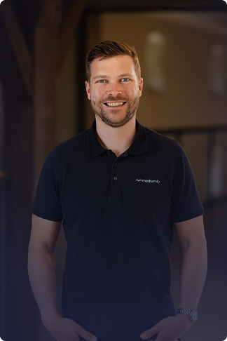 Mann mit kurzem Haar und Bart lächelt, trägt ein dunkles Polohemd mit Medservio-Logo.