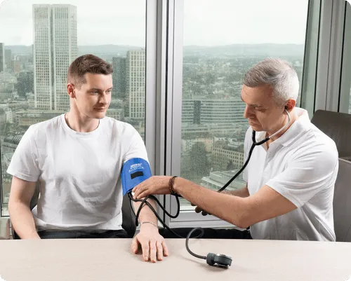 A healthcare professional measuring a young man's blood pressure in a high-rise office with city view.