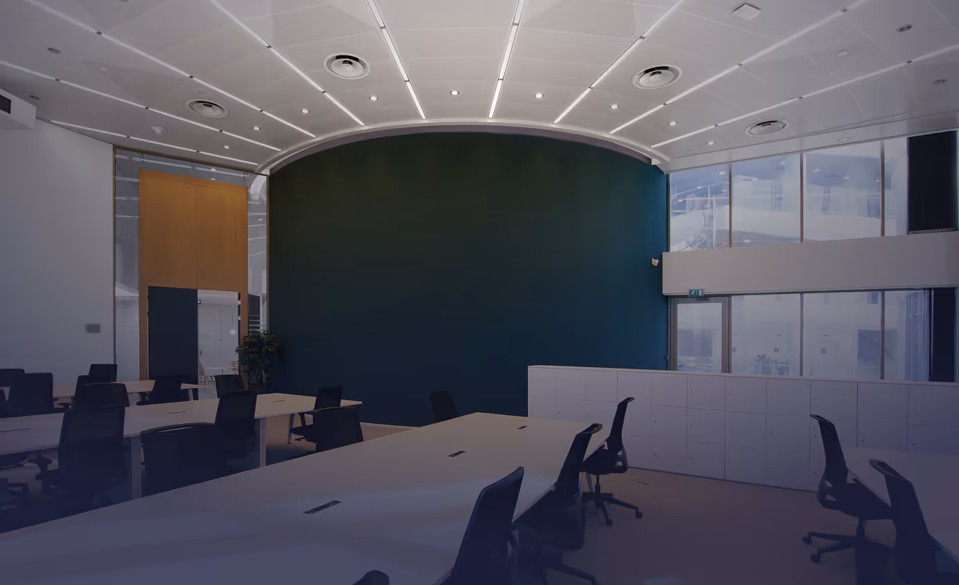 Moderner Besprechungsraum mit weißen Tischen, schwarzen Bürostühlen, großer grüner Wand und Oberlichtern.