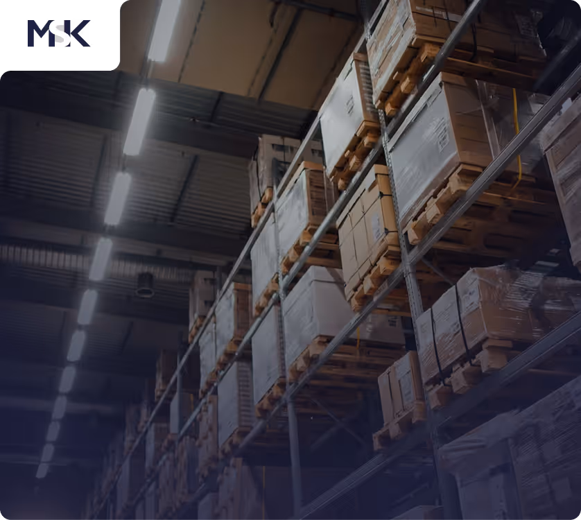 Regale in einem Lagerhaus mit gestapelten Kartons auf Holzpaletten unter Deckenbeleuchtung.