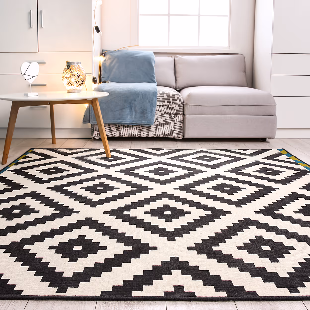 Black and white geometric patterned rug in front of a light gray sectional sofa and a round wooden coffee table in a bright living room.