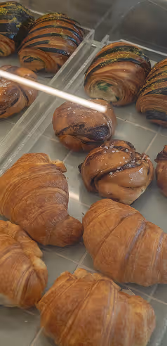 Display case with assorted pastries including croissants and chocolate-glazed buns on trays.