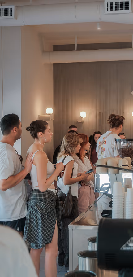 People standing in line and waiting to order at a modern coffee shop with warm lighting.