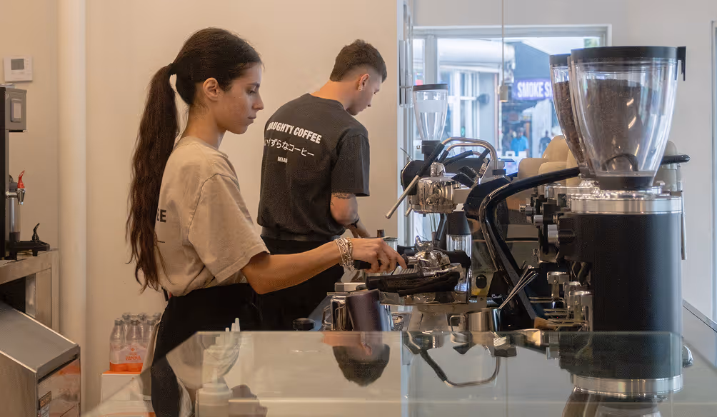 Two baristas preparing coffee behind a counter with espresso machines in a modern cafe.