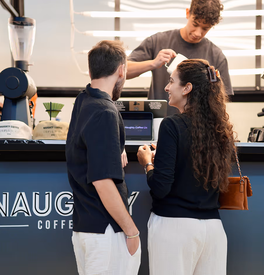 Barista pouring milk for a man and woman ordering coffee at Naughty Coffee bar.