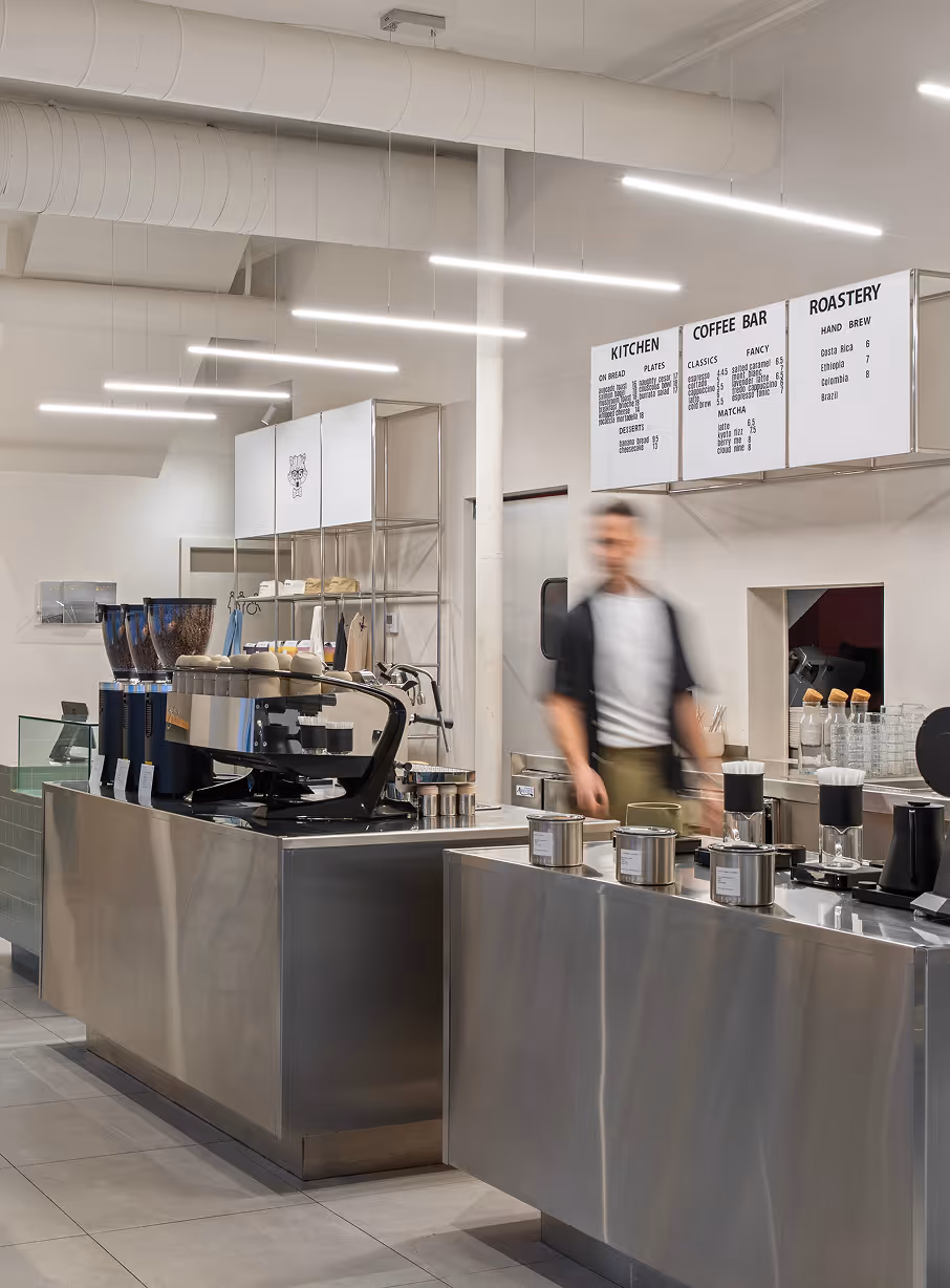 Modern coffee shop interior with stainless steel counters and menu boards above the barista.