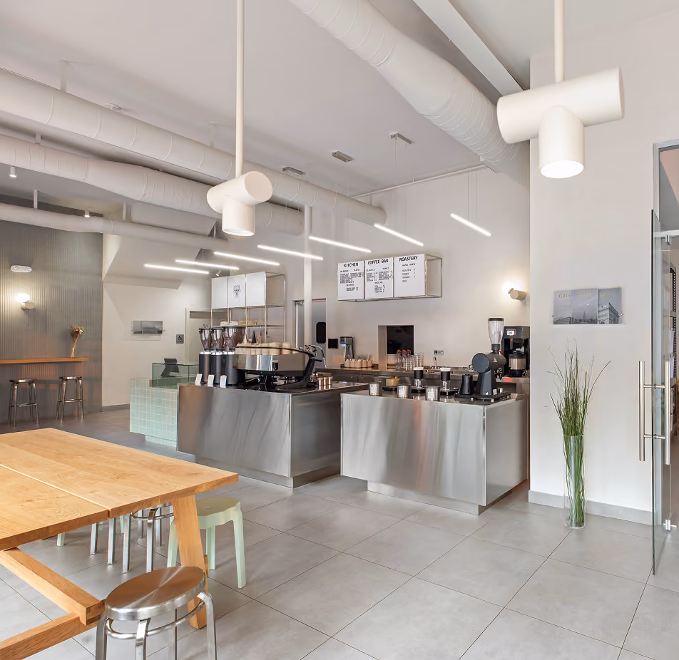 Modern coffee shop interior with stainless steel counters, wooden tables, stools, and minimalist decor.