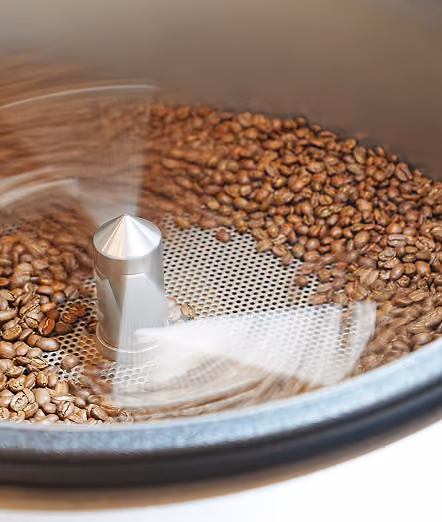 Coffee beans being roasted in a machine with a rotating arm stirring them.