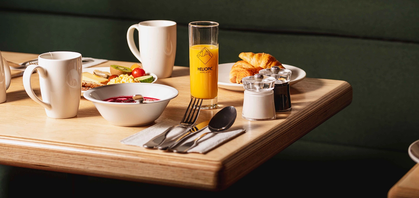 Petit déjeuner sur une table en bois avec jus d'orange, croissants, bol de soupe ou compote, assiette de fruits et tasses blanches.
