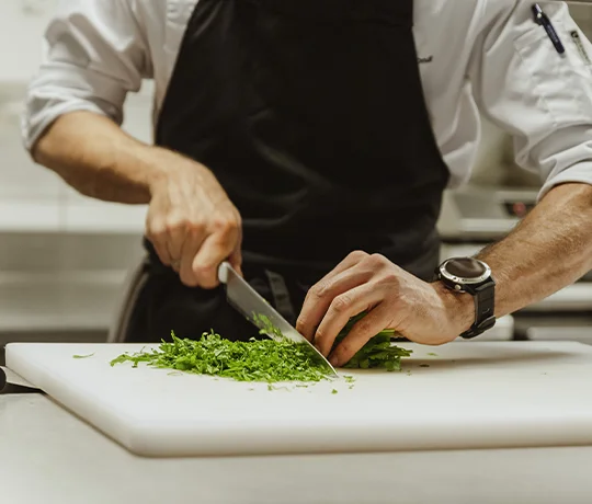 Membre du la cuisine découpant des brins de ciboulette avec un couteau, dans la cuisine du retsaurant Akashon de l'Heliopic Hotel & Spa à Chamonix