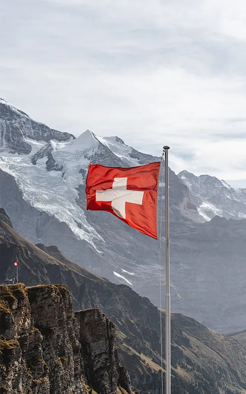 Le drapeau suisse flottant dans les airs depuis le sommet du Männlichen, avec en arrière-plan le massif de la Jungfrau et ses sommets enneigés.