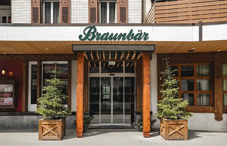 Façade du Braunbär Hotel & Spa avec au centre l'entrée principale sous un porche en bois et décoré de deux sapins