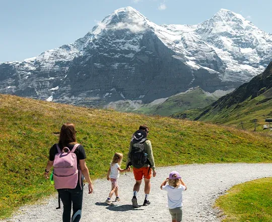 Une famille marchant sur les chemin de randonnée autour de Wengen durant le printemps et avec l'Eiger et le Mönch à l'horizon.