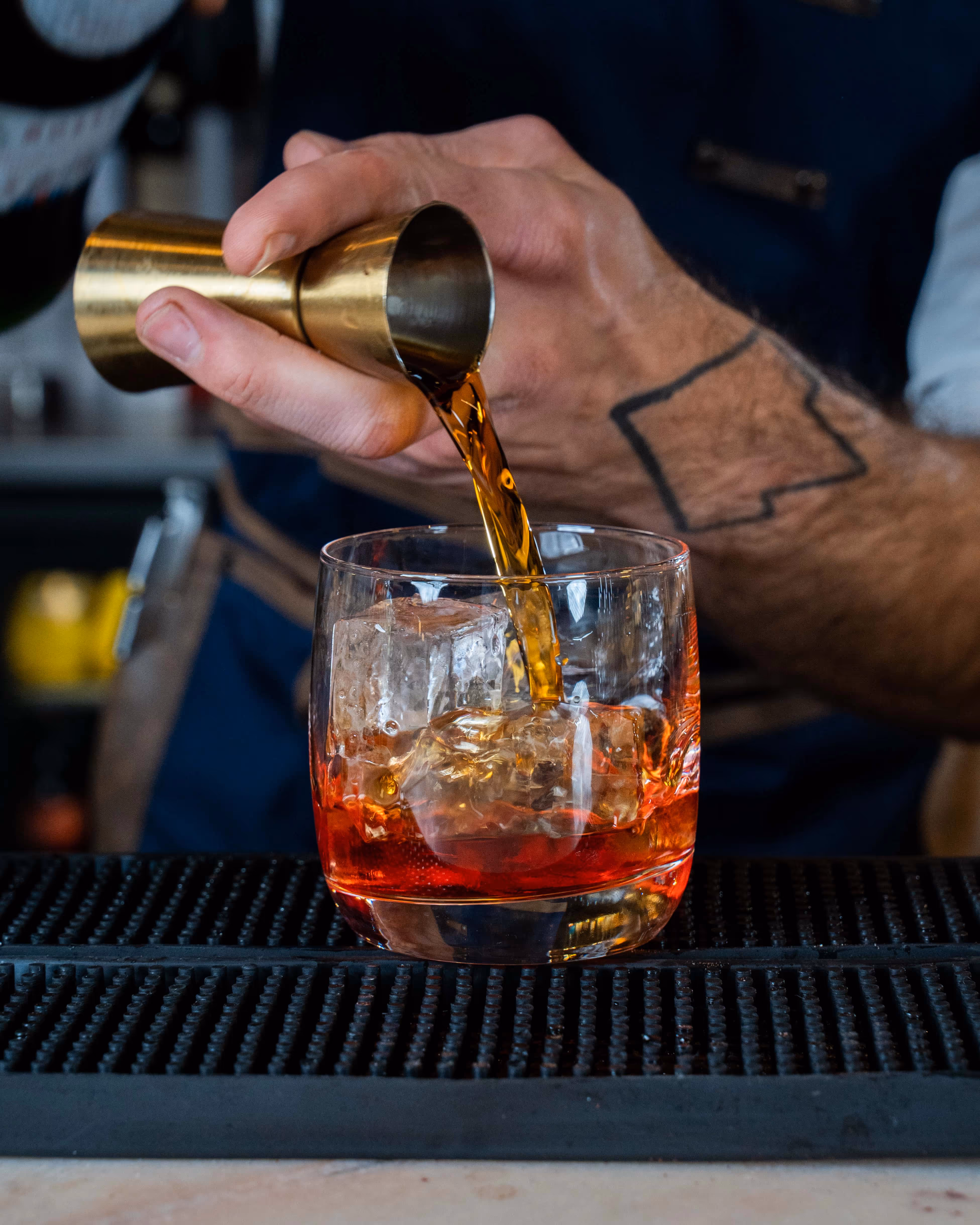 Un bartender préparant un cocktail en versant de l'alcool dans un verre à mixer