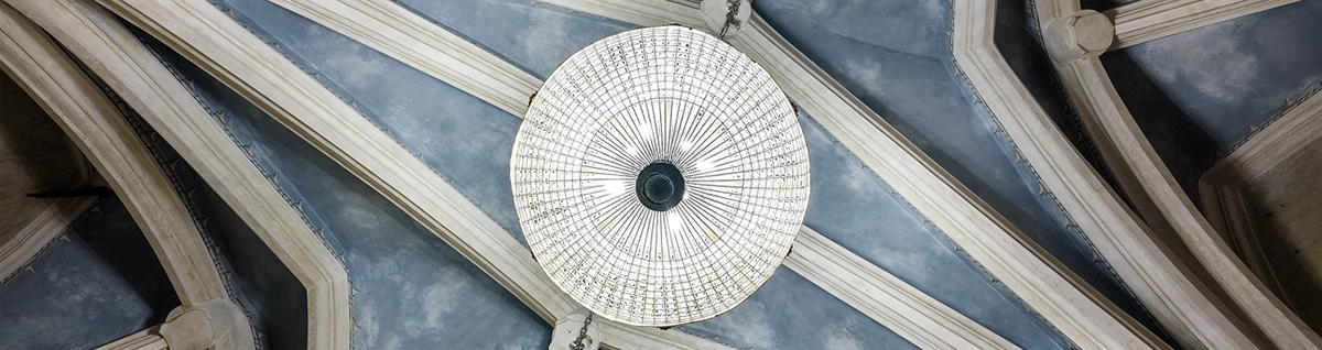 Spojrzenie z dołu na ozdobne, szare sklepienie sali restauracyjnej z łukowymi żebrami i podwieszonym okrągłym, kryształowym żyrandolem.