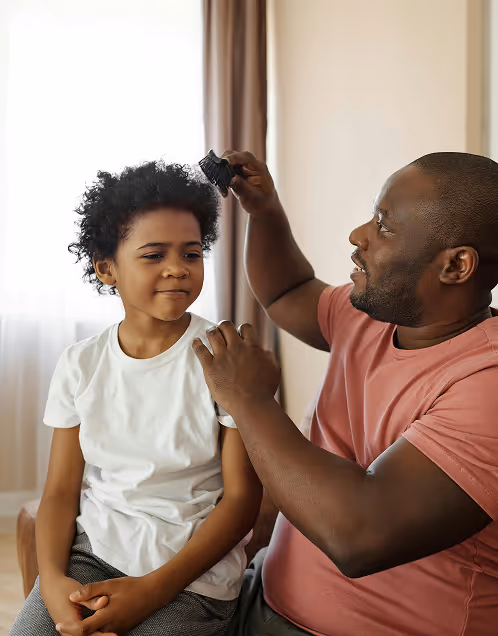 A man using hair clippers to cut a young boy's curly hair indoors.