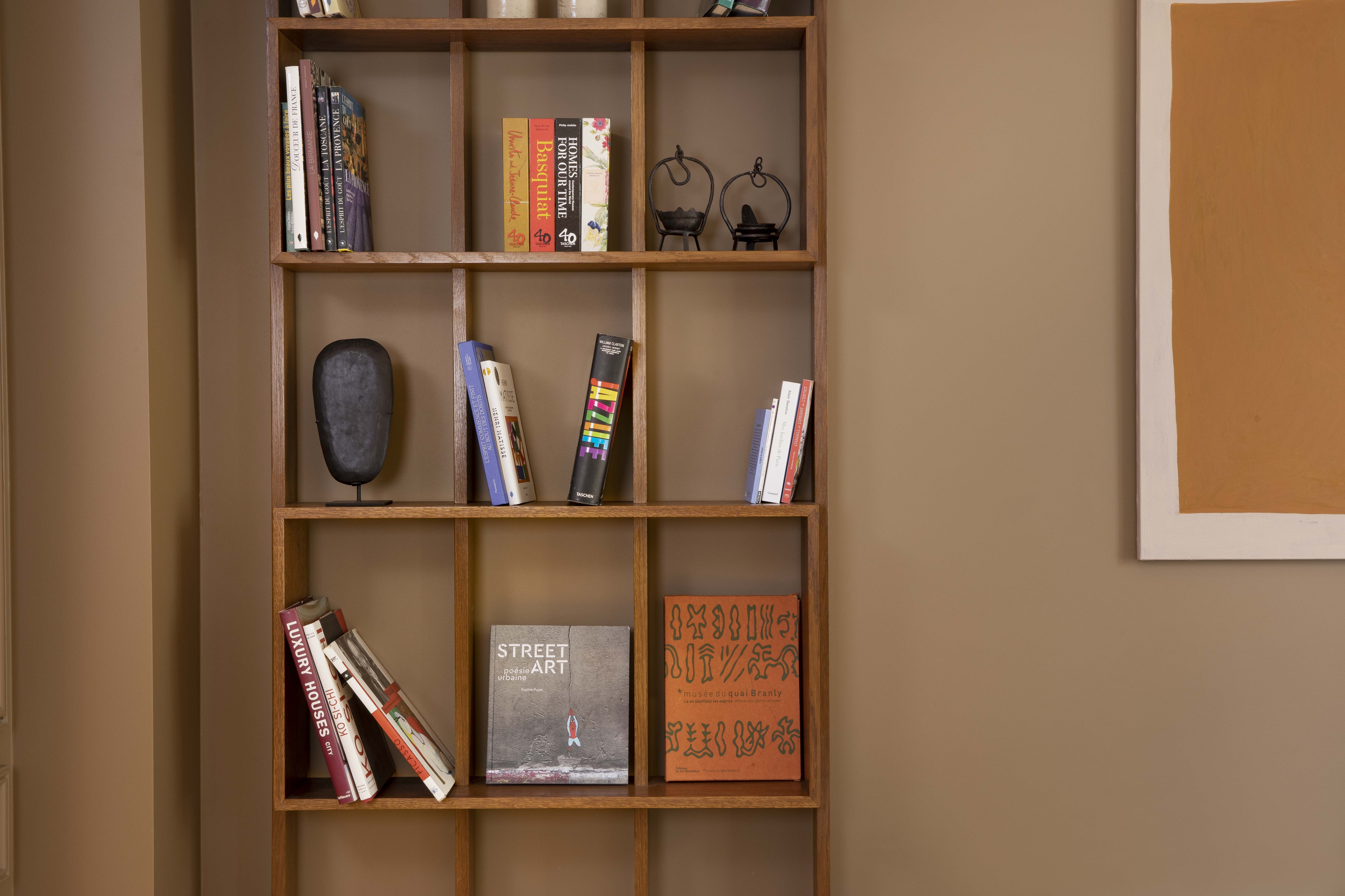 Wooden shelf with books and decorative items against a beige wall next to a framed brown painting.