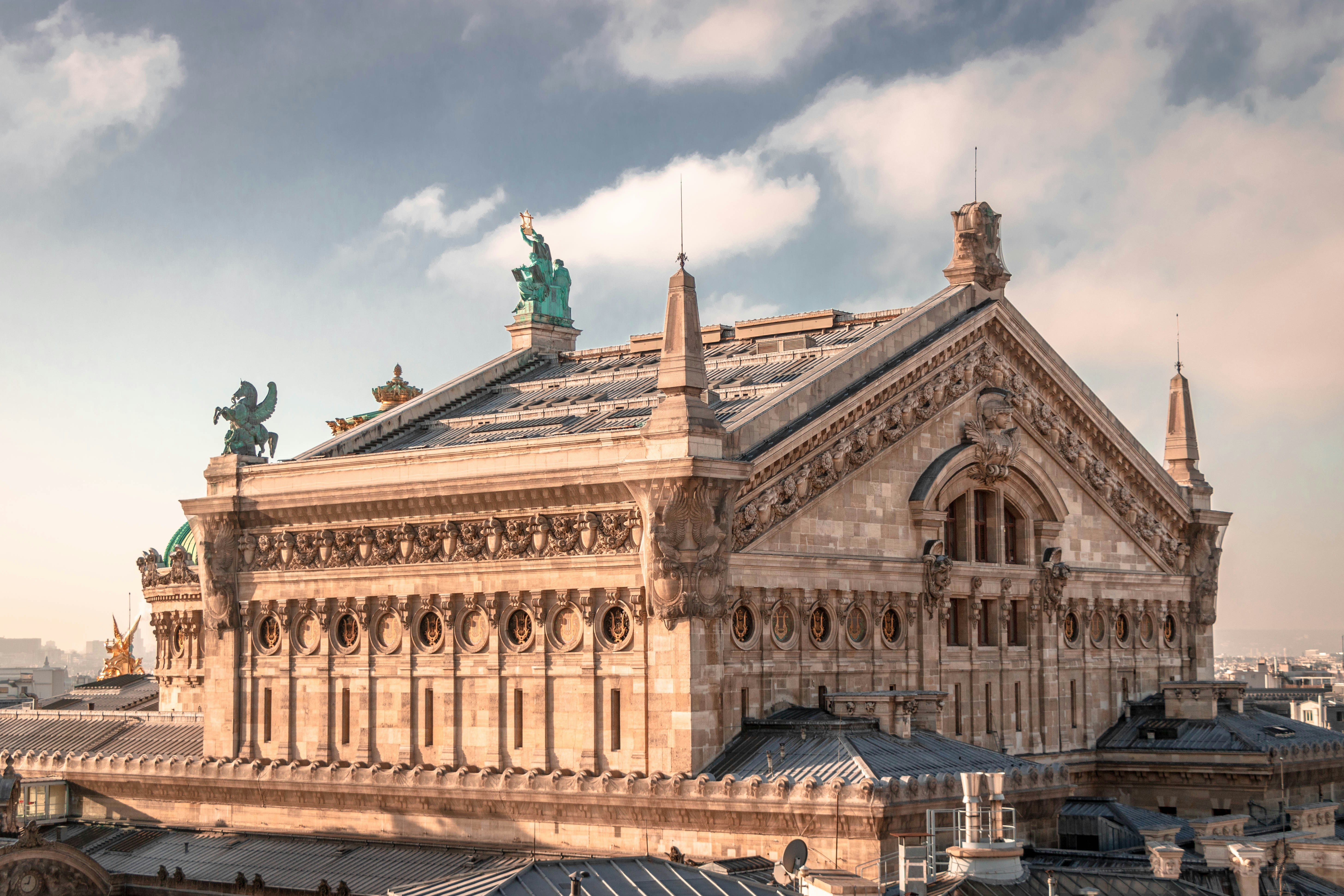 Ornate stone facade and zinc roofs of the Palais Garnier under a clear sky in Paris.