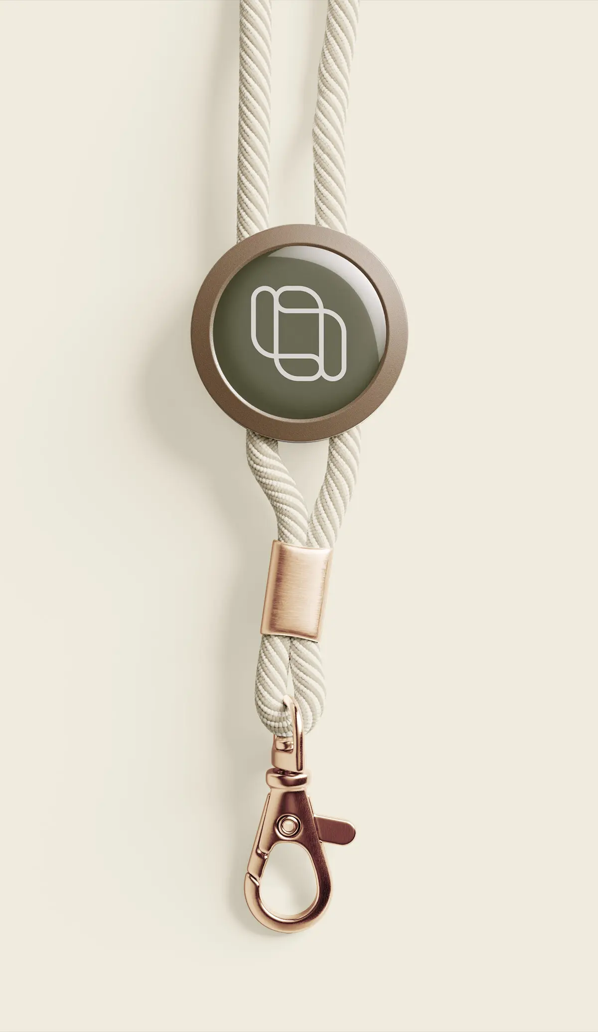 Nøkkelbånd i beige med rund brun flate med hvitt abstrakt logo samt gullfarget metallkrok.