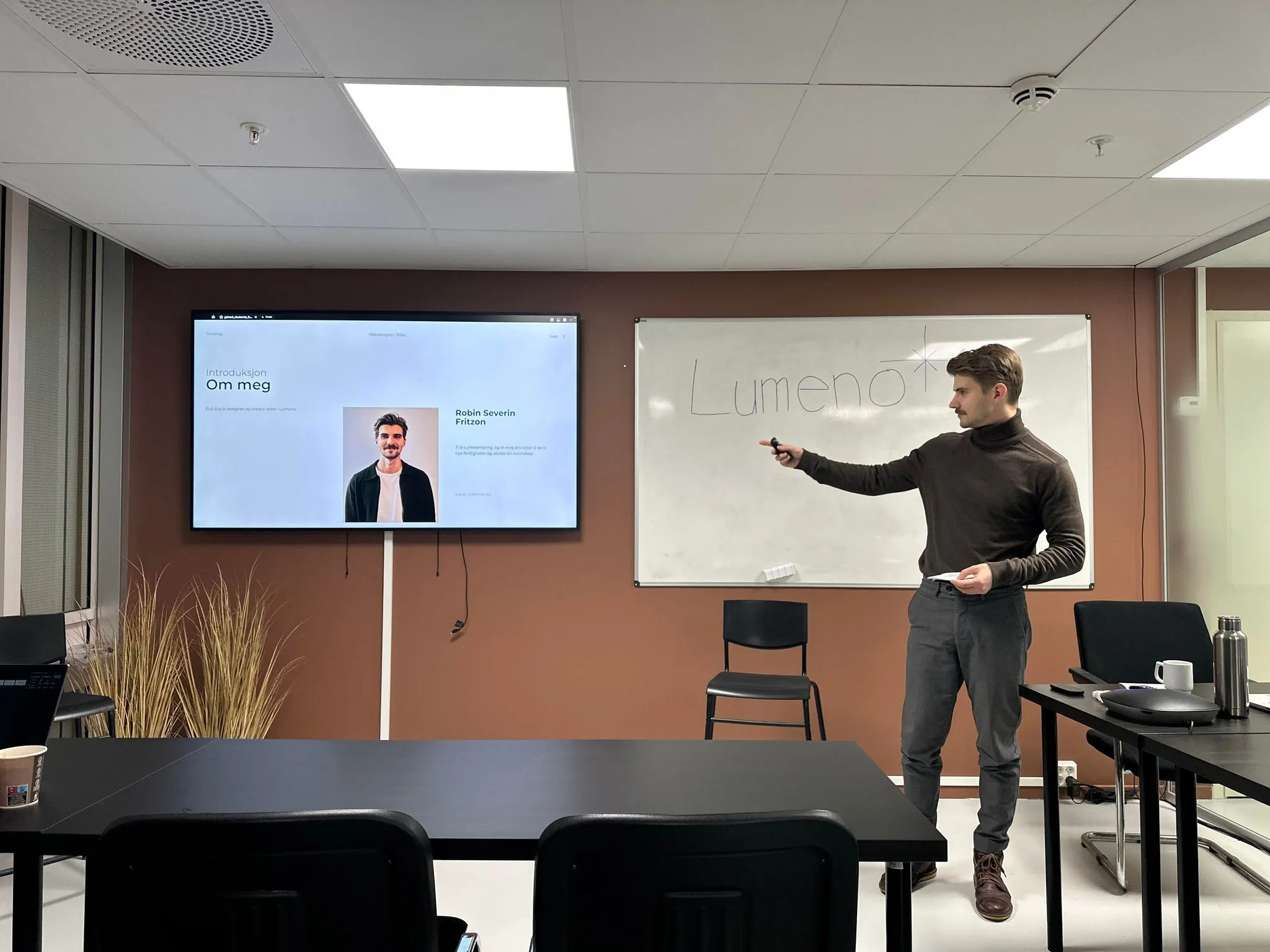 Robin står foran TV som viser presentasjonen og introduserer seg selv