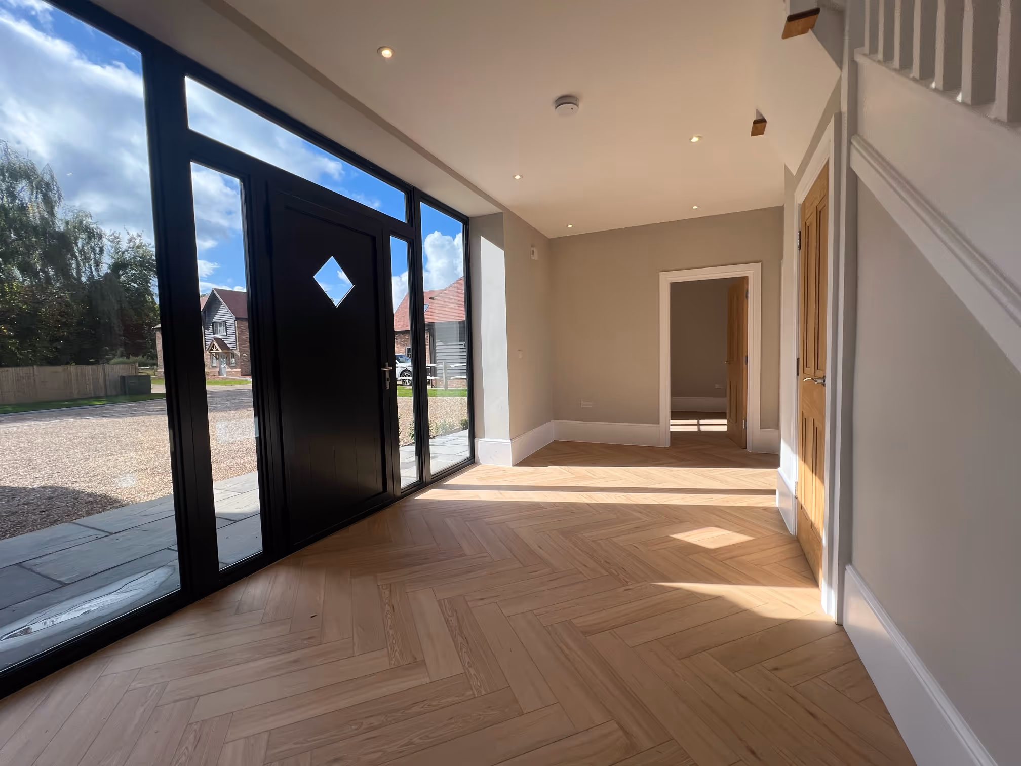 Bright modern entryway with large black-framed glass door and windows, light wood herringbone floor, and neutral walls.