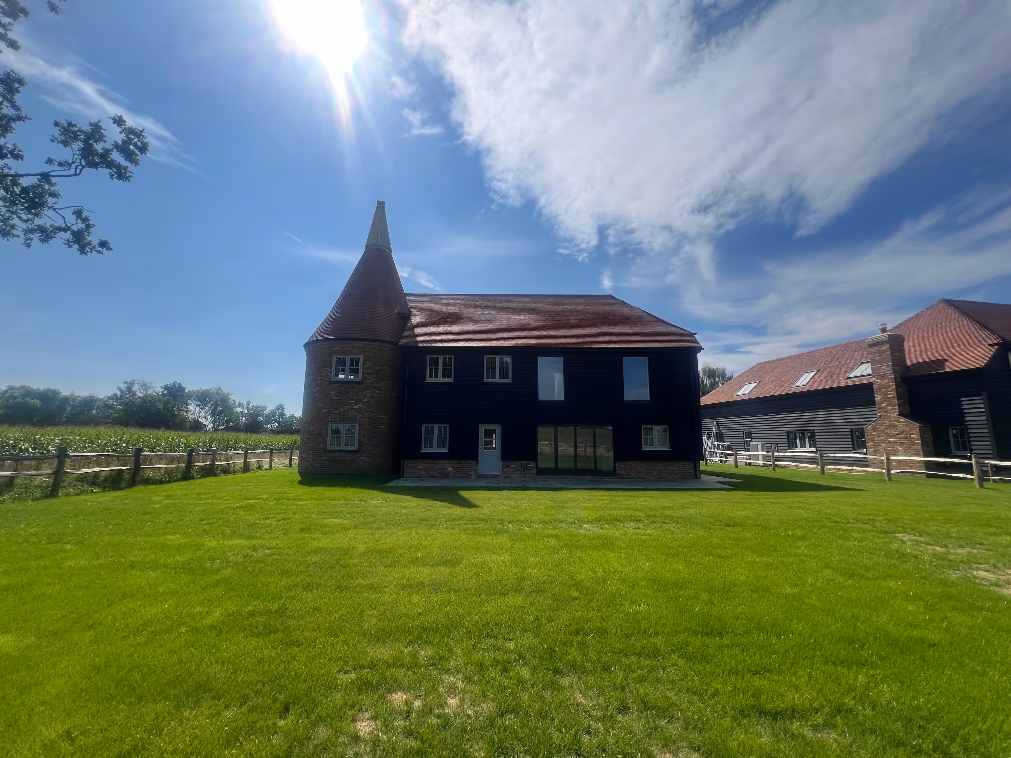 Black house with a conical brick turret and red roof under a bright sunny sky, surrounded by green grass and a wooden fence.