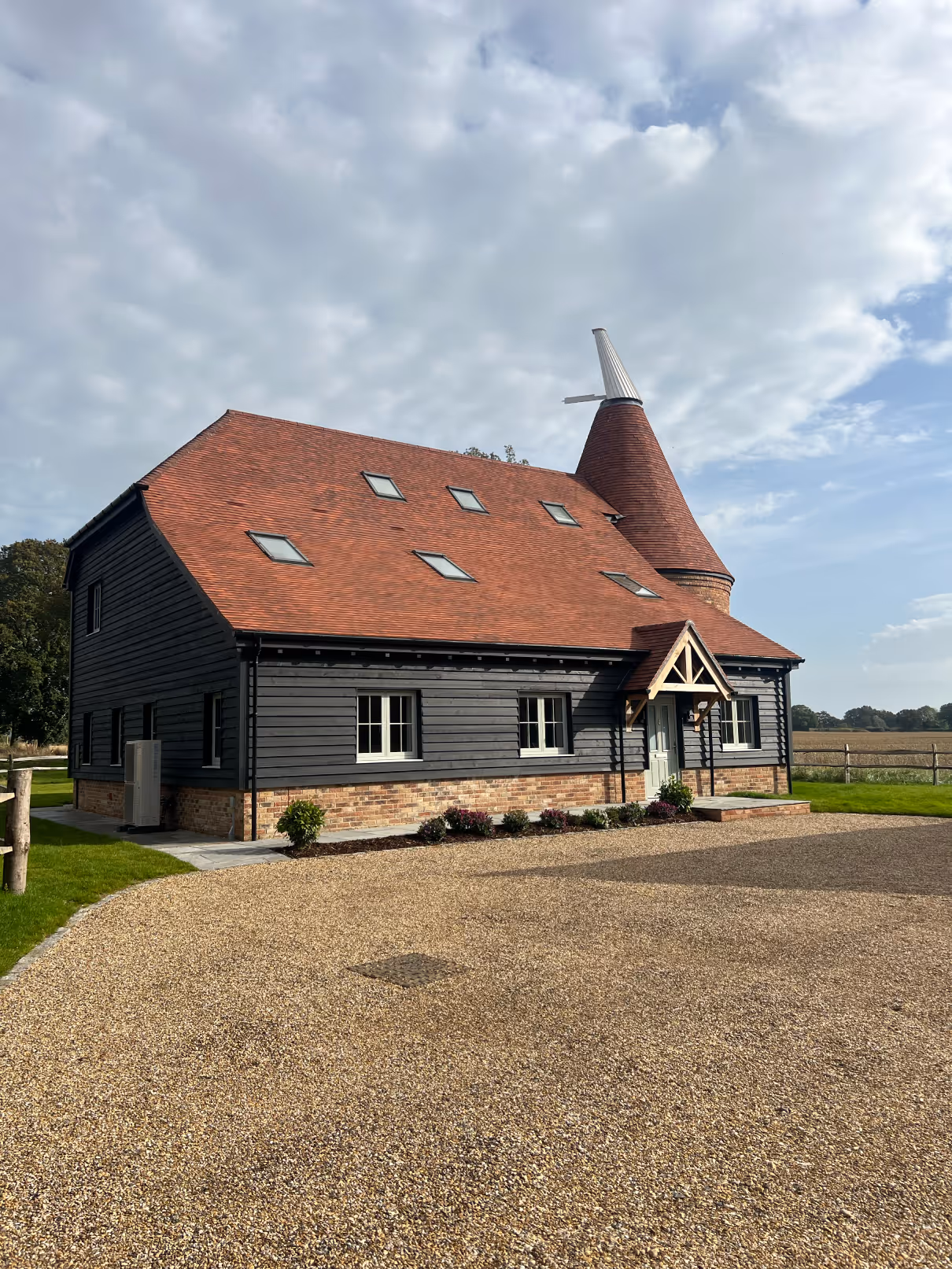 Large rustic house with a red tiled roof, black wooden siding, and a distinctive conical tower against a partly cloudy sky.
