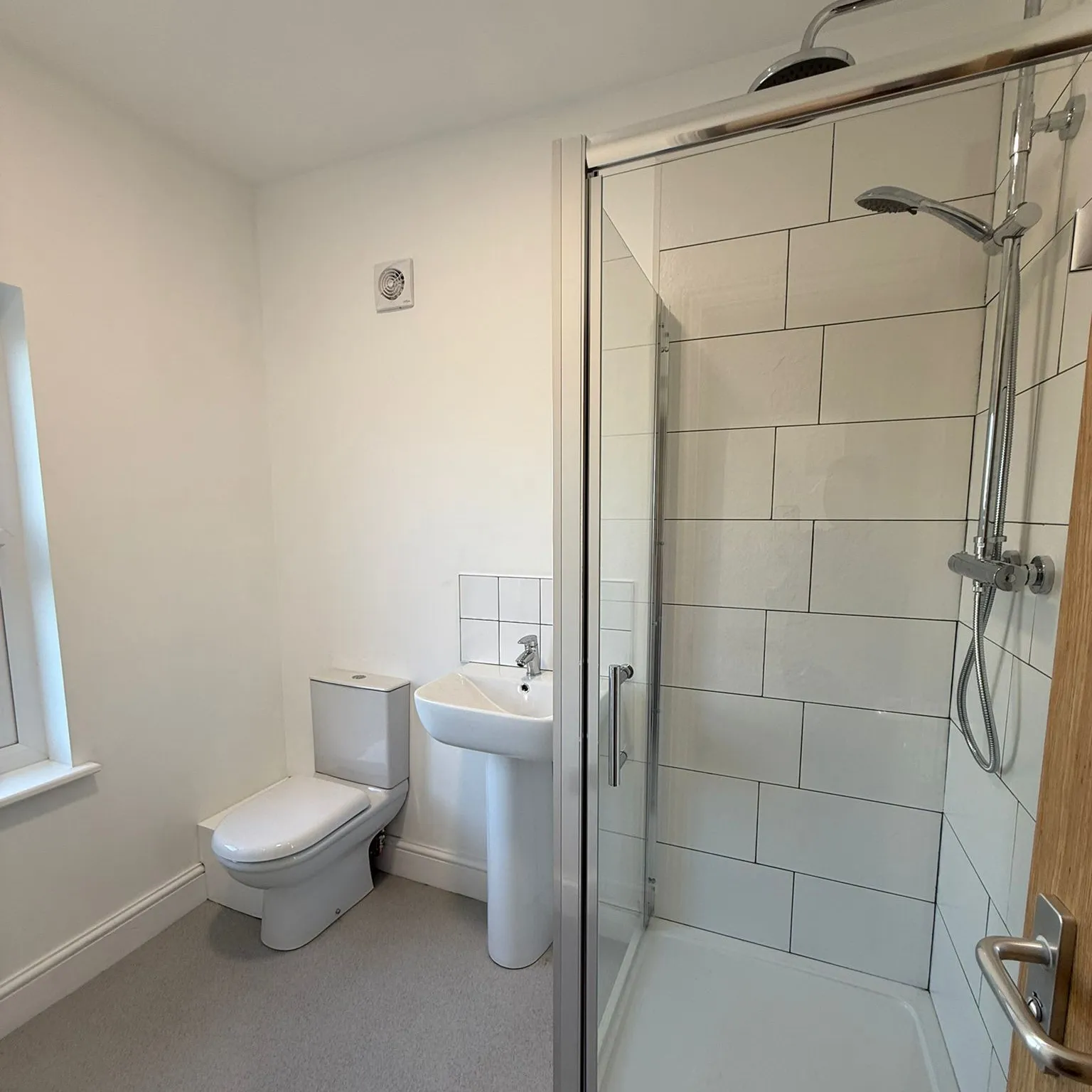 Minimalist bathroom with white toilet, pedestal sink, and tiled glass-enclosed shower with dual showerheads.