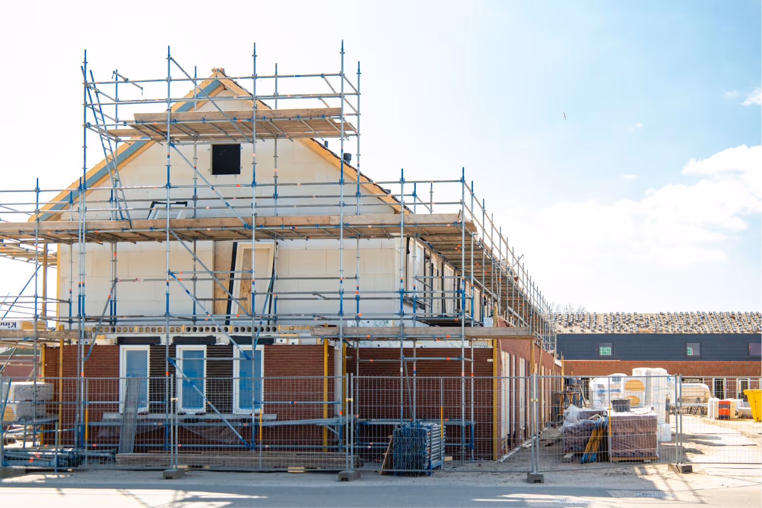 A residential building under construction with scaffolding surrounding the exterior and construction materials on site.