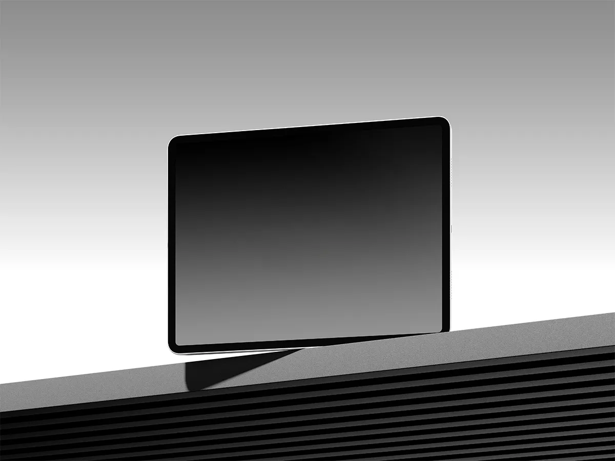 Tablet with black screen balanced on the edge of a textured surface against a gradient gray background.