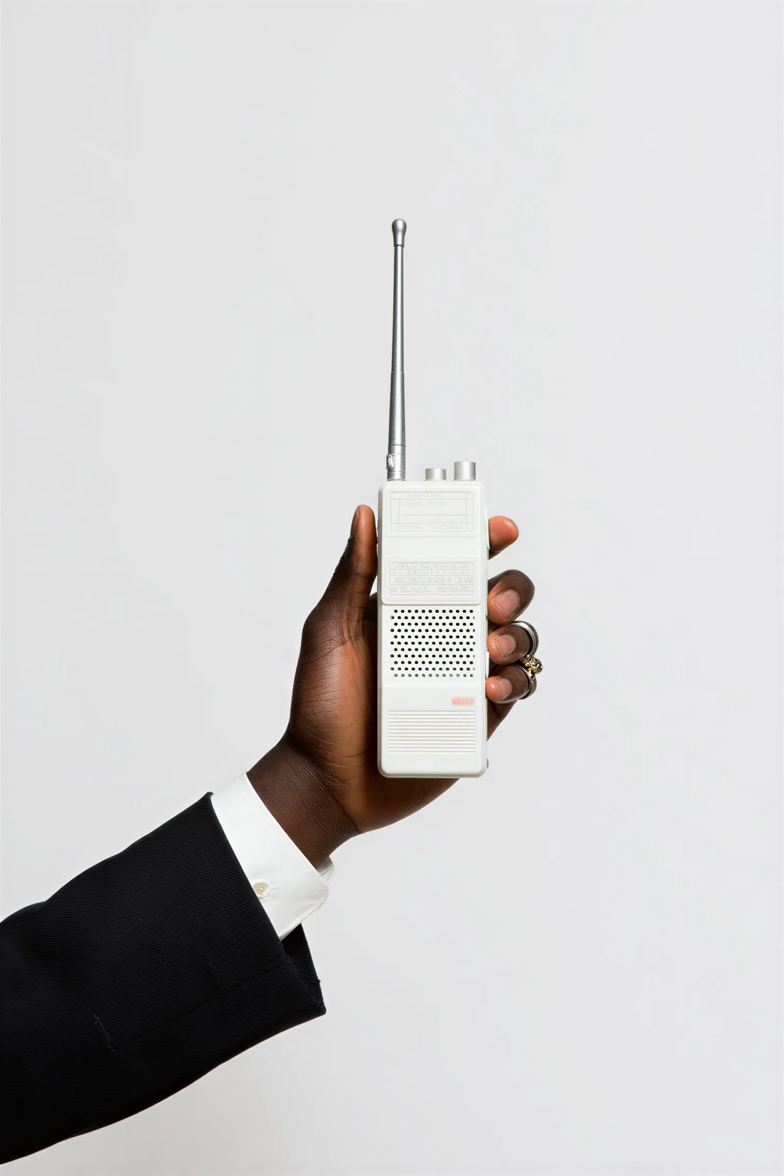 Hand of a person wearing a black suit holding a vintage white walkie-talkie with an extended antenna.