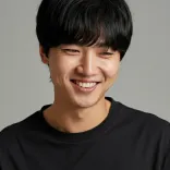 Smiling young man with black hair wearing a black shirt against a gray background.
