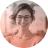 Smiling young woman with glasses and short curly hair wearing a peach-colored top.