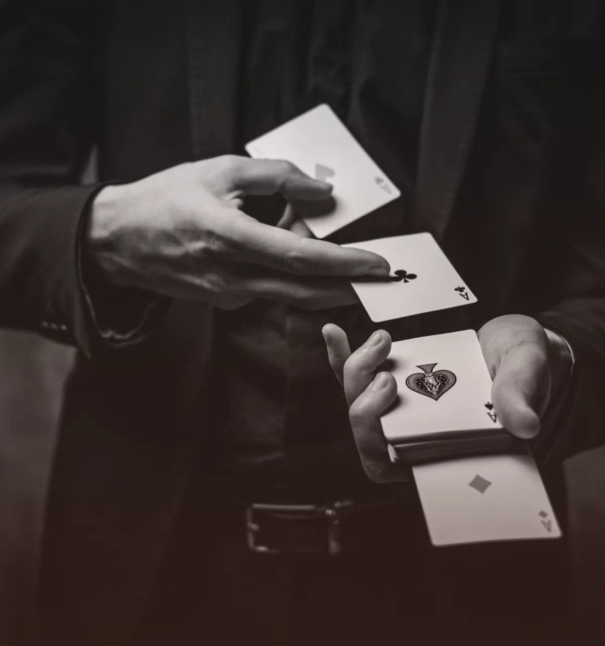 Person in dark clothing performing a card trick with aces of hearts, clubs, spades, and diamonds visible.