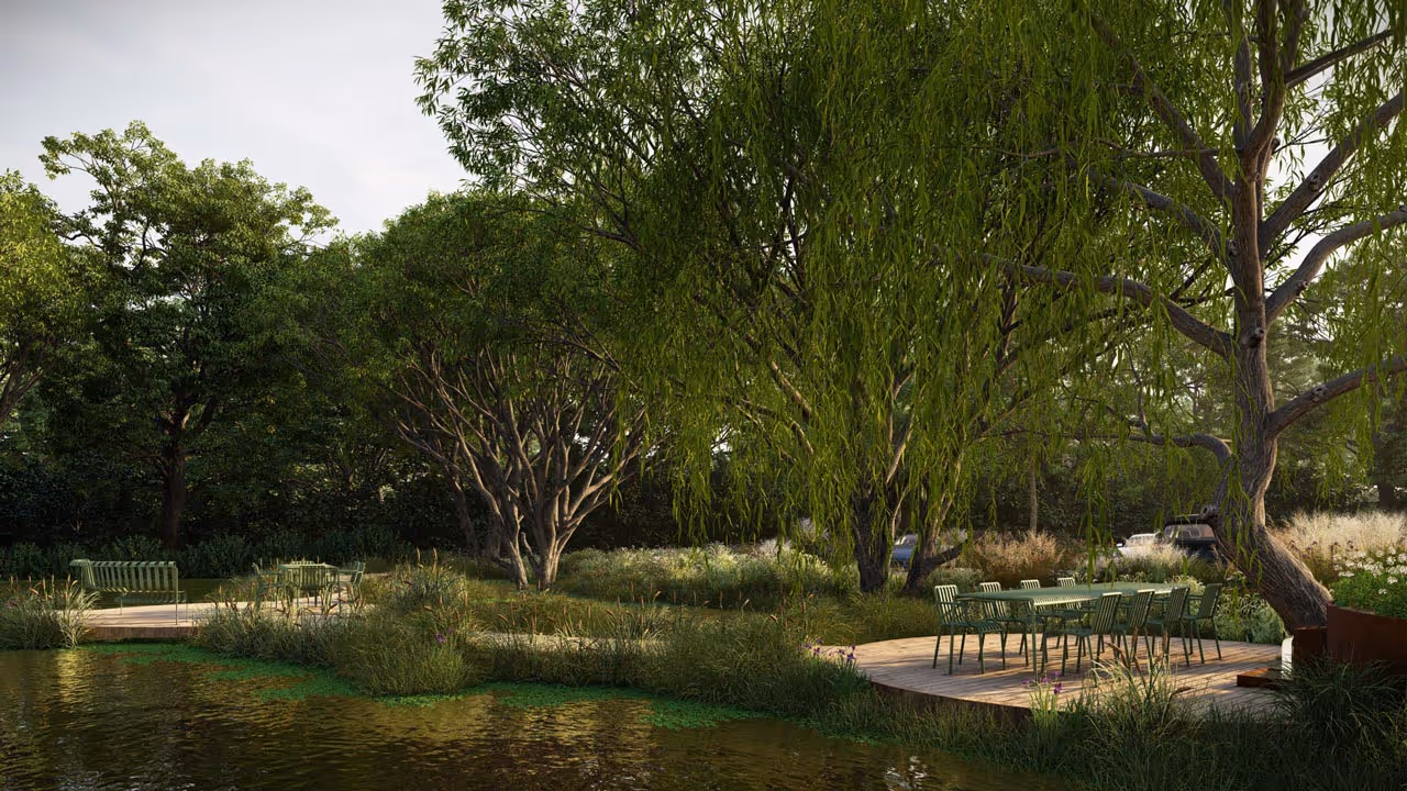 Outdoor seating area with green chairs and tables on wooden decks surrounded by lush trees and vegetation beside a calm body of water.