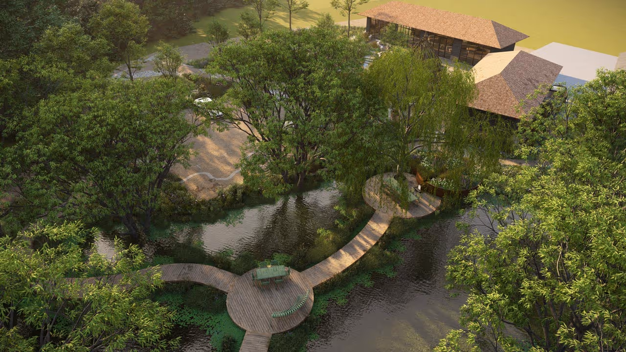 Aerial view of a serene garden with wooden paths and circular decks over water surrounded by lush green trees and two modern buildings in the background.