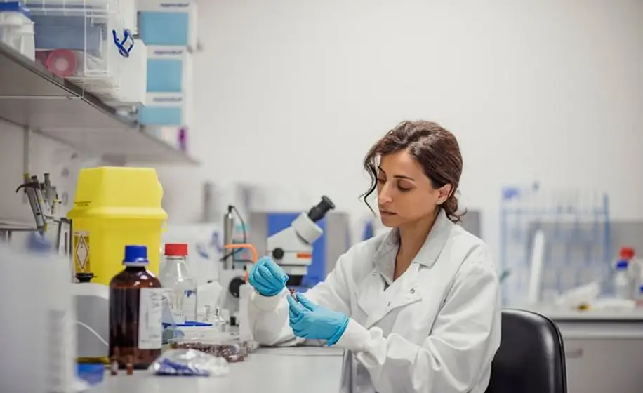 Scientist in lab coat examines samples using laboratory equipment