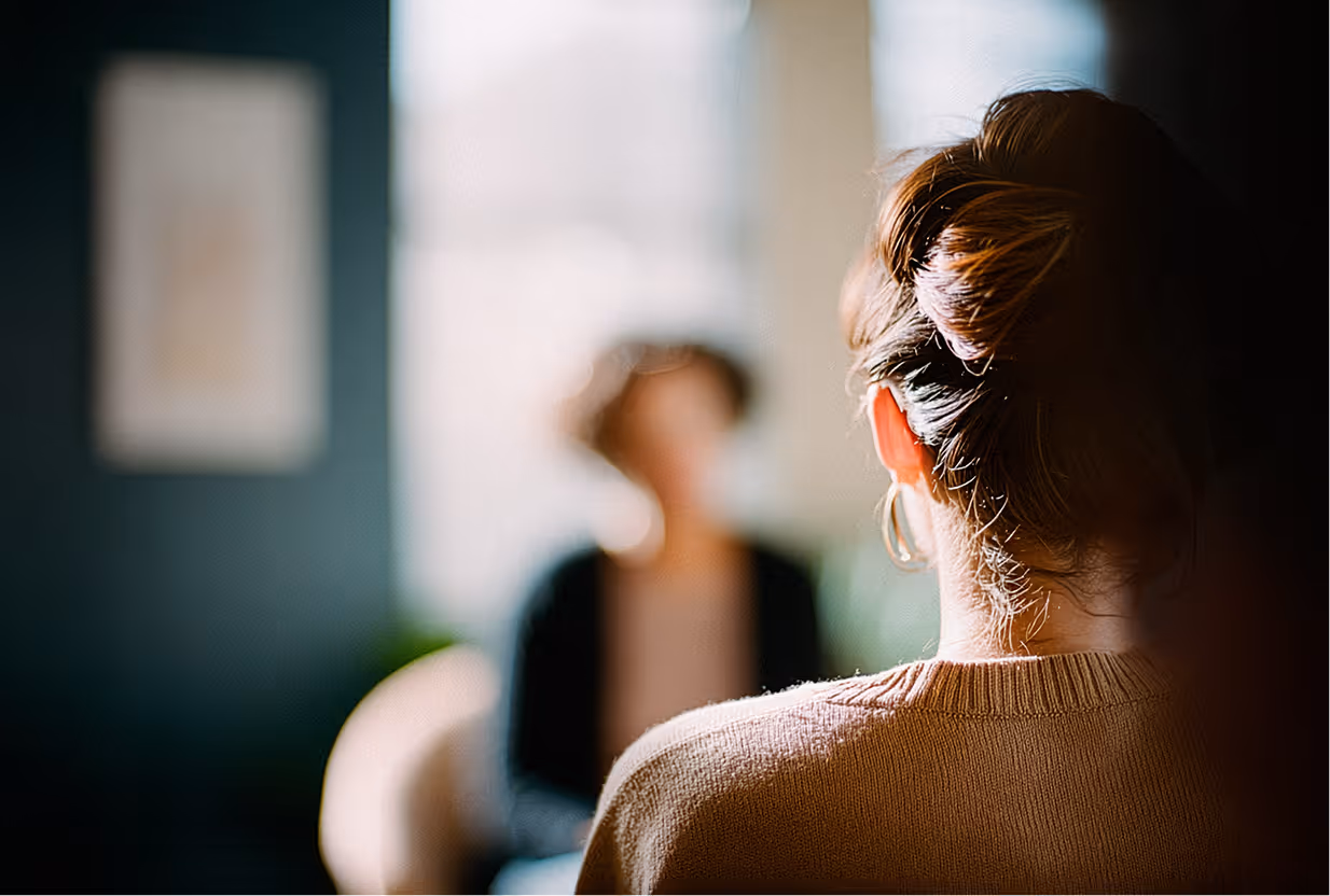 Kvinna med uppsatt hår i samtal med en annan person i ett ljust rum.