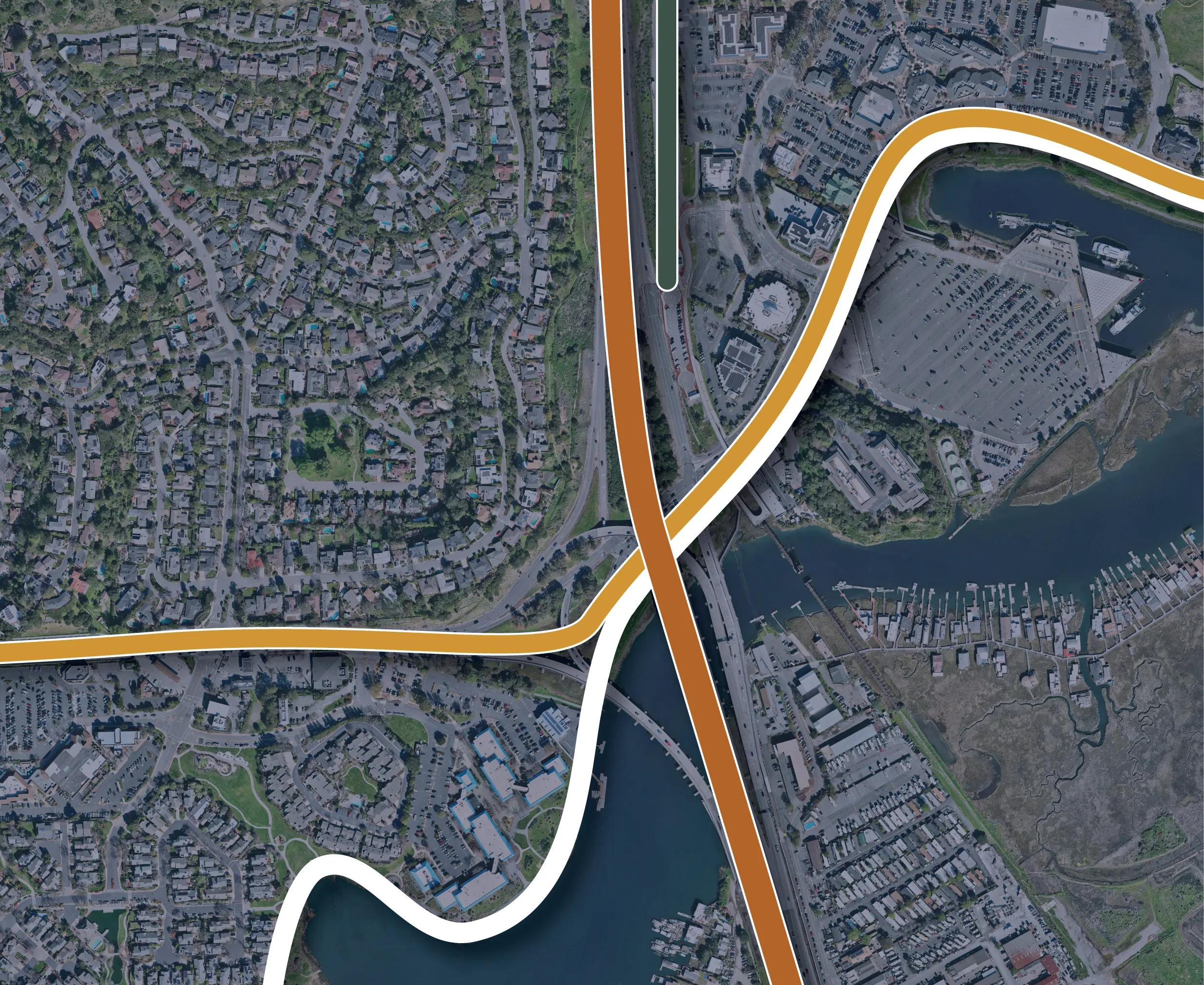 Aerial view of a suburban area with numerous residential houses and roads, intersected by two major highways with orange and white lines marking their paths, passing over a body of water and a marina with docks.
