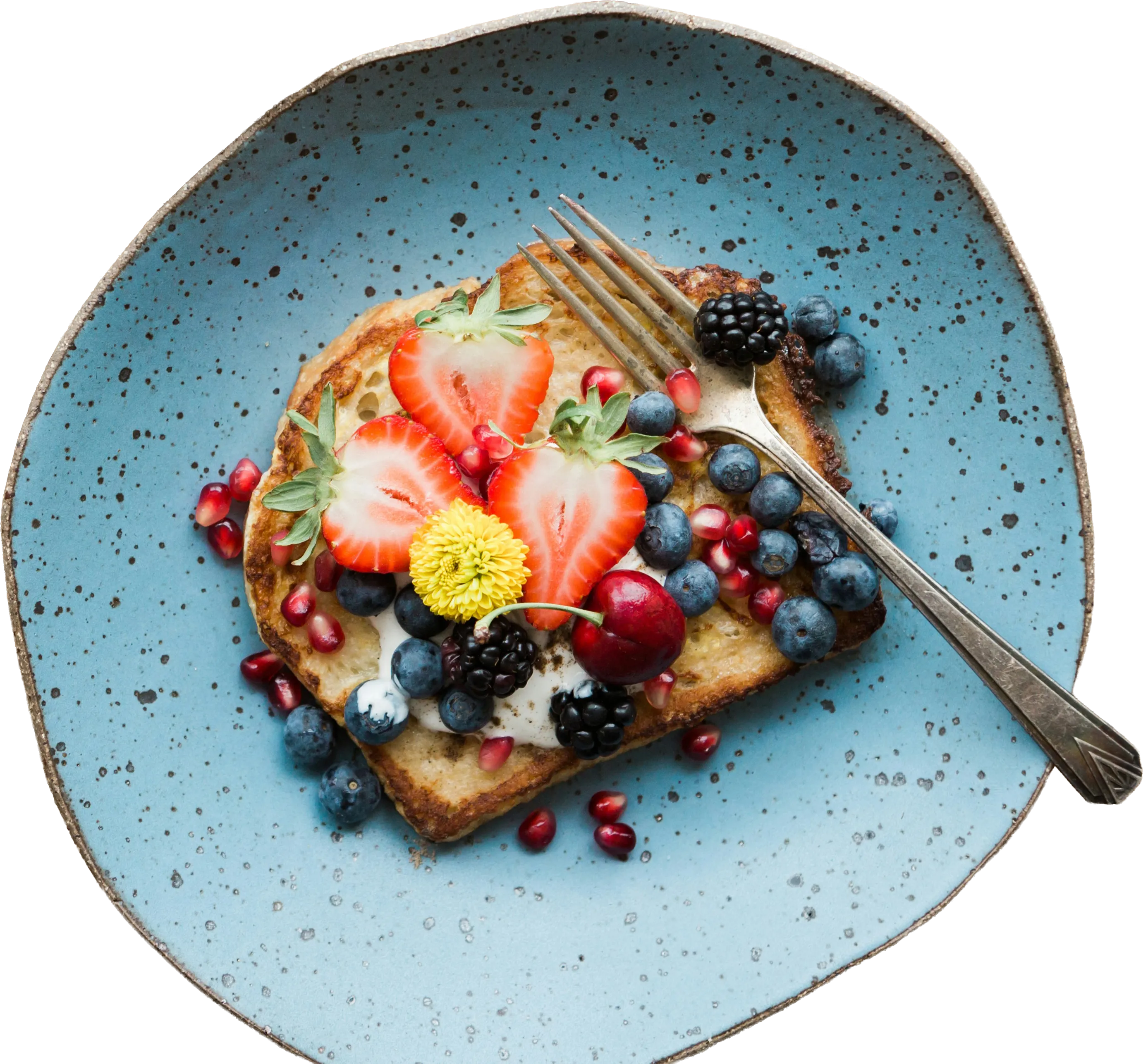 Slice of French toast topped with strawberries, blueberries, blackberries, pomegranate seeds, a cherry, cream, and an edible yellow flower on a blue speckled plate with a fork.