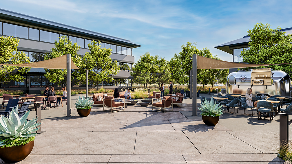 Modern outdoor courtyard with seating areas including brown cushioned chairs around fire pits and blue dining chairs. People are sitting and standing, socializing under partial sun shades. Green trees and large potted plants enhance the space. A silver food truck is parked on the right side near a modern building with large windows.