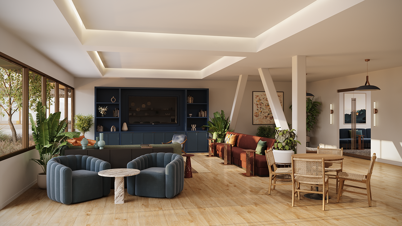 Modern, spacious living area with wooden flooring, featuring two blue velvet armchairs around a small wooden table, a large blue shelving unit with a built-in TV, a green sofa, a brown sofa with accent pillows, several potted plants, a round wooden dining table with four wicker chairs, and large windows letting in natural light.