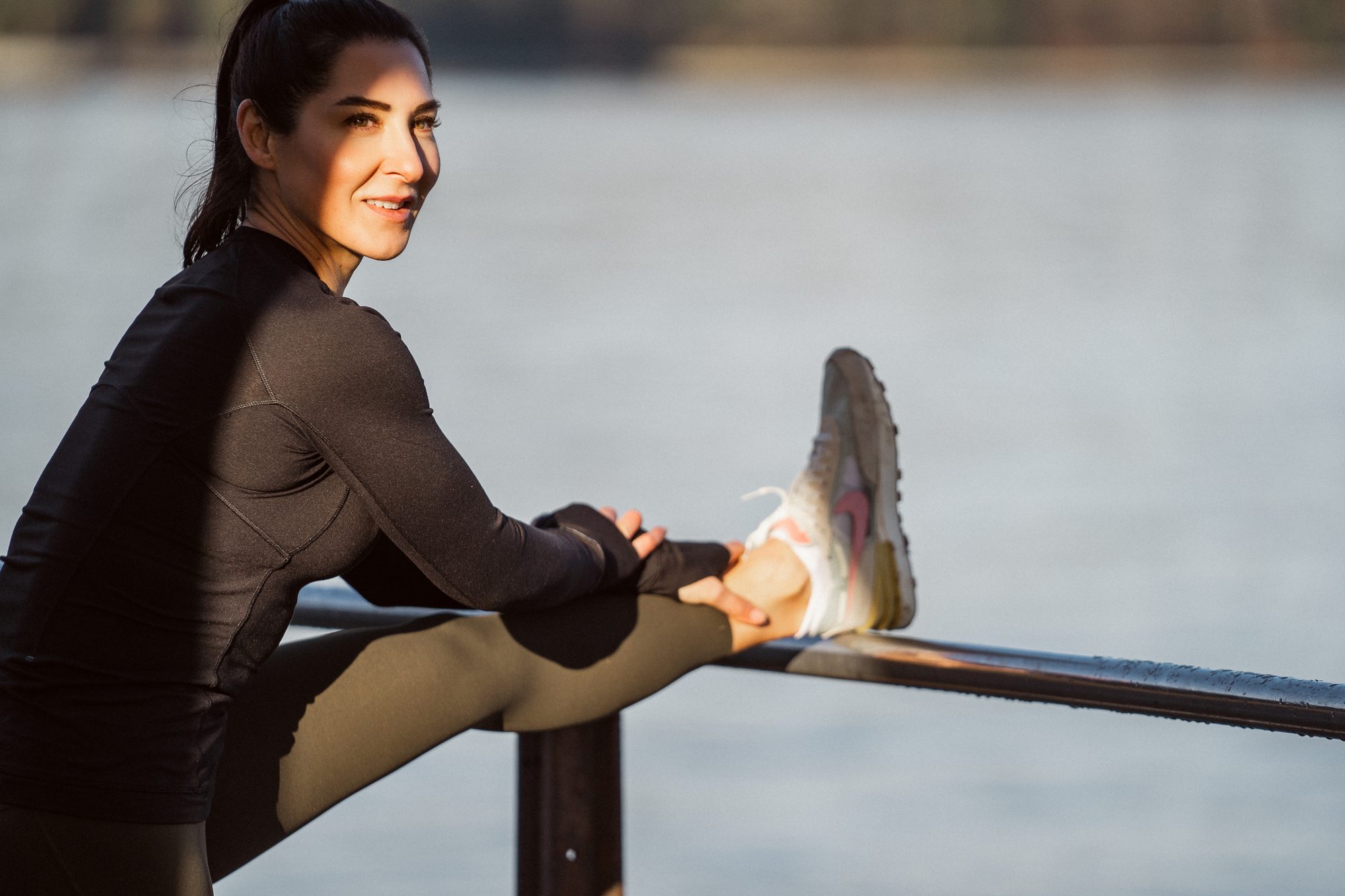 Smiling woman stretching on a railing by the water