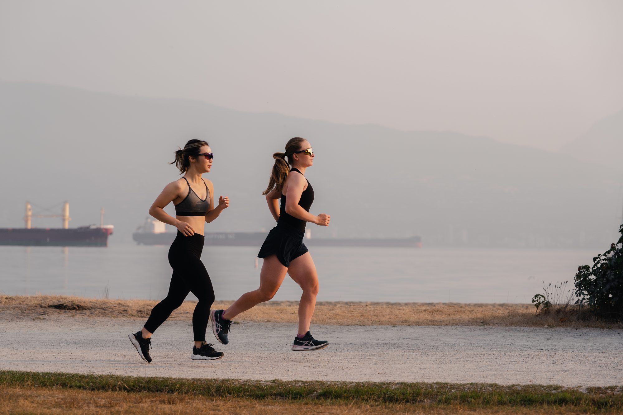 Two women running side by side along a misty beach path