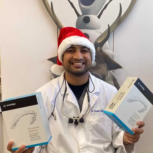 Dr. Patel in a Santa hat holding Invisalign aligner boxes