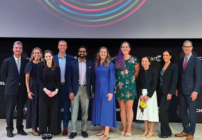 Group of ten diverse professionals standing in front of a black backdrop with colorful circular logos.