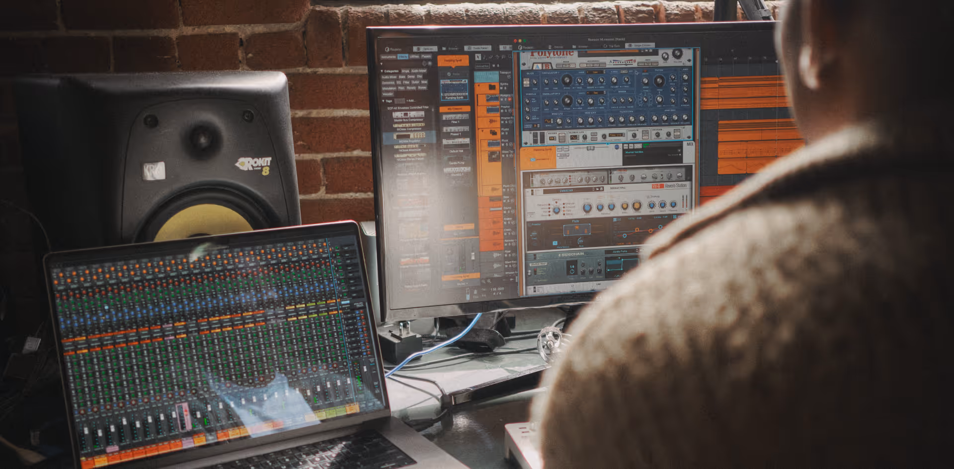 Person working on music production software with a laptop, studio monitor, and external screen.