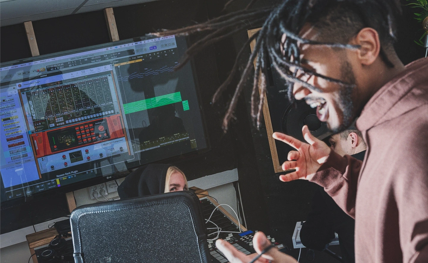 Artists working on music production in a recording studio with a large screen showing audio software.