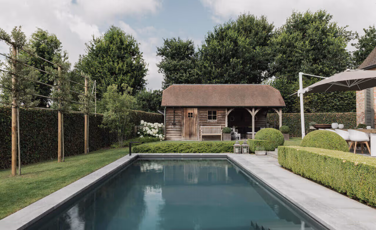 Outdoor pool with rectangular shape in a garden featuring trimmed hedges and a wooden shed.