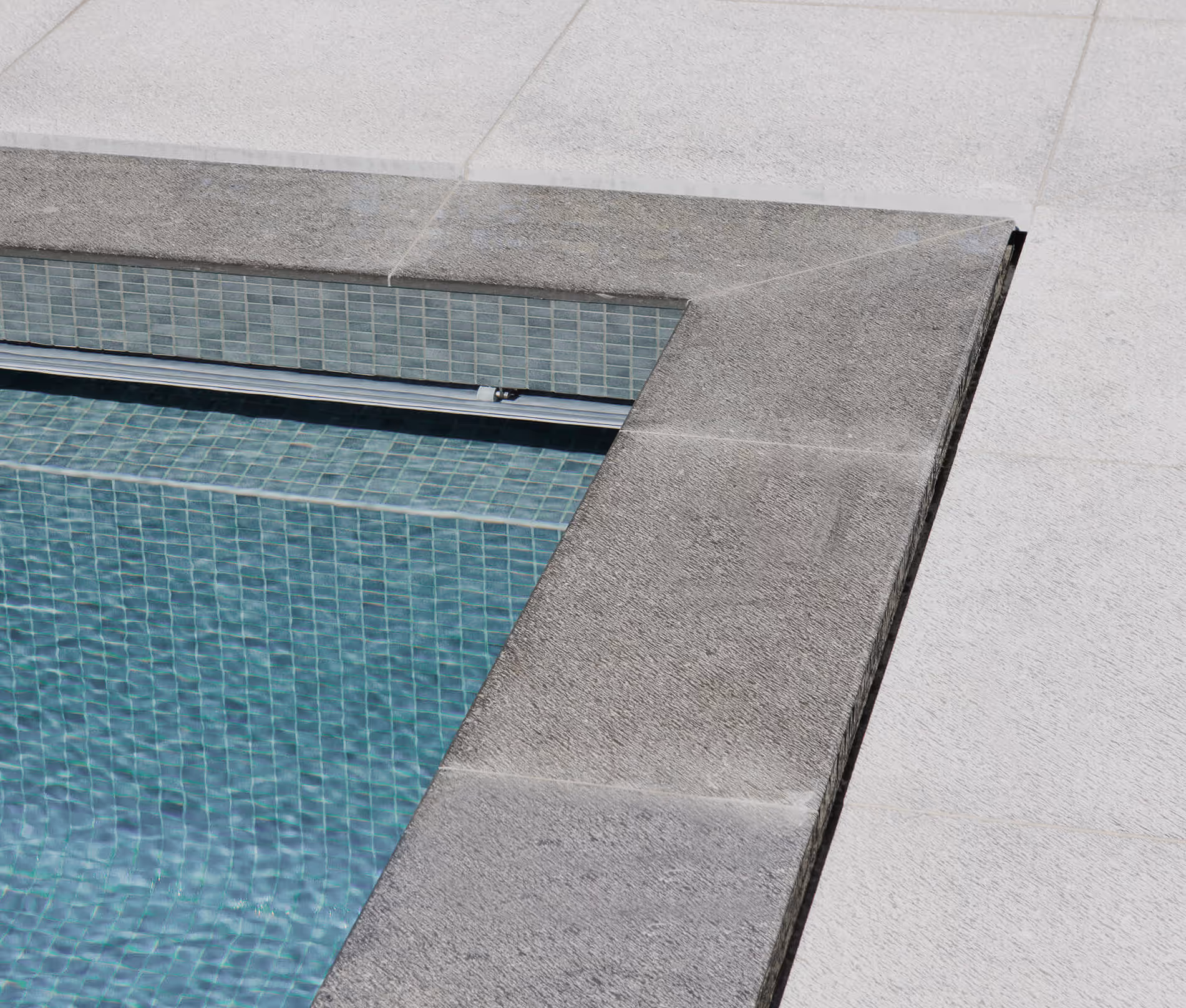 Close-up of a pool corner with textured stone edging and light blue tiled interior surface.